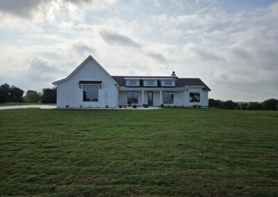 Two-story modern farmhouse with white siding, black metal roof accents, and expansive green lawn