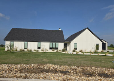 One-and-a-half story farmhouse-style home with dormer windows and dark shutters on a large open lot