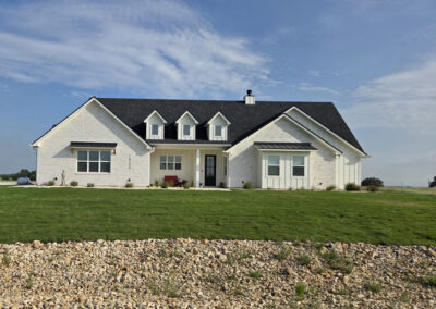 Single-story white farmhouse with multiple dormers, columned front porch, and wide green pasture frontage