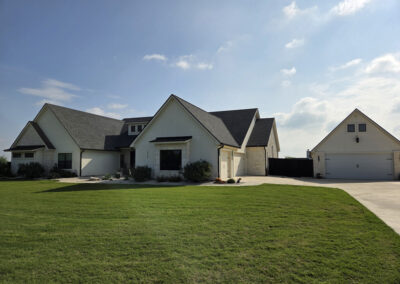 Modern farmhouse with light stone base, dark gabled roof, and white siding accents on a green corner lot