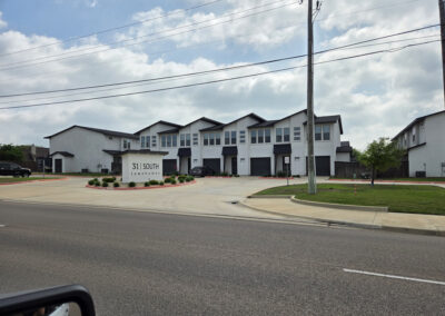 Modern two-story townhome row with light siding, dark trim, and concrete driveways in a streetscape view