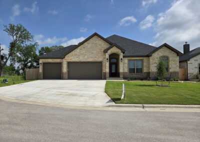 Tan brick single-story home with central gable, two-car garage, and traditional Central Texas curb appeal