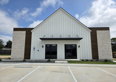 Modern commercial barn-style building with white board-and-batten siding, dark metal roof, and oversized overhead door