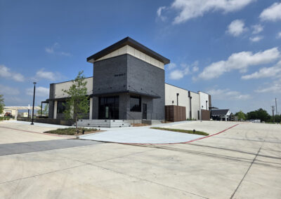 Two-story modern commercial building with dark stucco exterior and full-height glass entry