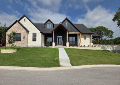 Light brick two-story home with prominent stone-arched entry and multi-gabled roofline on a corner lot