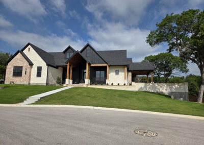 Stone and stucco custom home with covered front porch, dormer windows, and manicured landscaping
