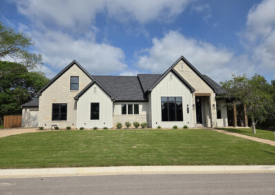 Tan brick and stone Hill Country-style home with steep gables, dark roof, and freshly poured driveway