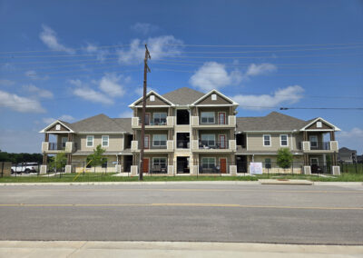Two-story multi-family residential building with painted siding, dormer windows, and landscaped frontage