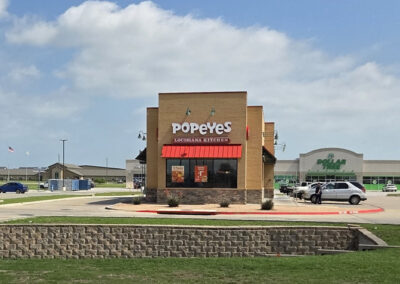 Popeyes restaurant with brick exterior, red and orange signage, and drive-through landscaping
