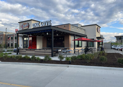 Multi-tenant retail building with red and tan stucco façade, awnings, and curbside parking