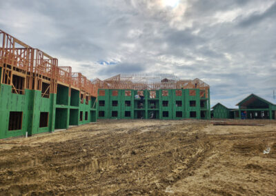 Multi-family residential building under construction, green-sheathed framing across multiple stories with roof trusses in place.