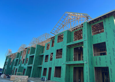 Multi-family residential building under construction, exposed wood roof trusses set over framed upper floors.