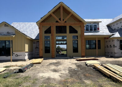 Custom home under construction featuring a dark heavy timber gable entry with exposed beams.