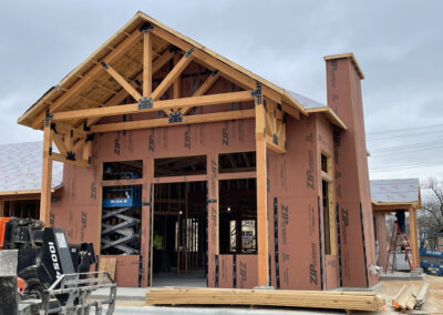 Heavy timber entry facade under construction, timber gable framing combined with stone and masonry.