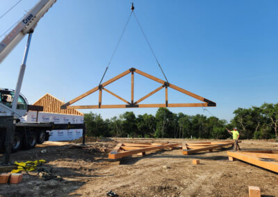 A fabricated wood truss being hoisted by crane into place at a construction site.