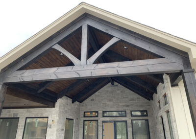 Dark-stained heavy timber gable truss with king post over a residential entryway, paired with stone masonry.